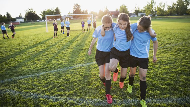 Middle school girl soccer players helping injured teammate off field