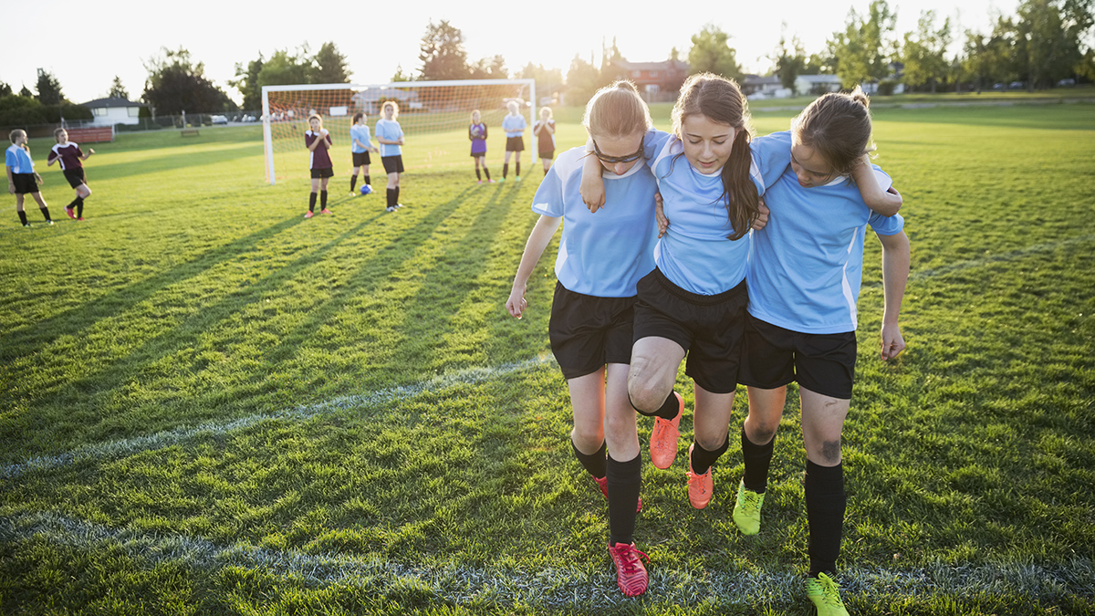 Middle school girl soccer players helping injured teammate off field